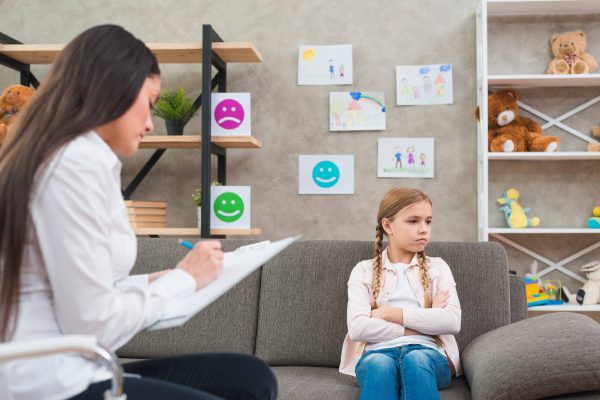 depressed-girl-sitting-sofa-with-female-psychologist-writing-note-clipboard-1-scaled